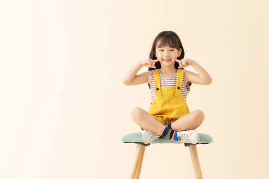 Happy Girl Sitting on Stool Pointing to Dimples and Smiling