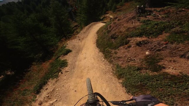 First-person POV footage of a mountain biker speeding downhill through a forest trail while following another cyclist, capturing fast movement, natural terrain and immersive outdoor action.