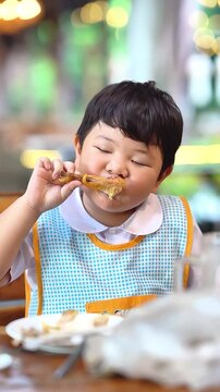 Happy Asian boy eating delicious Thai grilled chicken drumstick, slow motion.