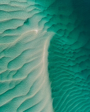 Aerial view of the turquoise waters and sandbanks of Moreton Bay, showcasing the intricate ripple patterns in the sand at Amity Point, Queensland, Australia.
