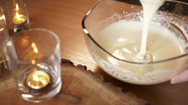 Lifting wire whisk from fluffy egg mixture in glass bowl with candles