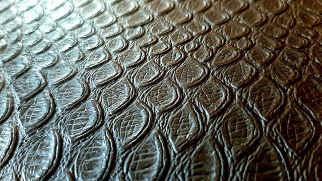 Dark embossed leather with snake scale pattern, close-up texture