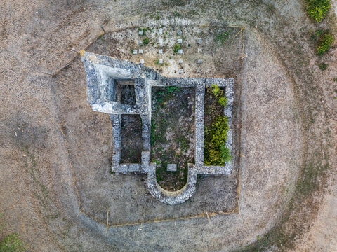 Aerial view of the medieval church ruins in Csabdi, Hungary, showing exposed stone foundations, an apsidal end, grave markers and dry grass around the historic site.