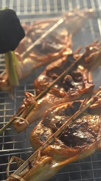 Slow motion of authentic Thai grilled chicken (Kai Yang) sizzling on charcoal grill.