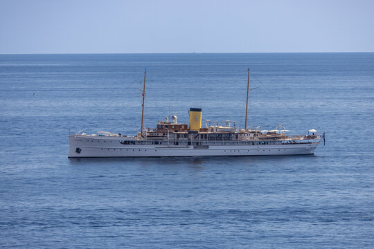 Aerial view of a classic white yacht with a yellow funnel sailing on the blue Mediterranean Sea off the coast of Monaco, Monaco.