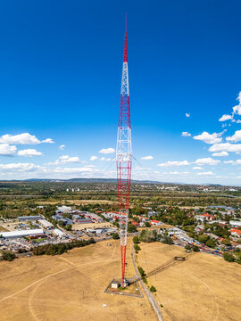 Aerial view of the Lakihegy radio tower, a tall red and white lattice mast with guy wires, standing in a field near the town of Szigetszentmiklos, Pest County, Hungary.