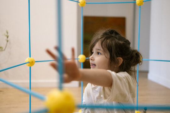 Little girl plays with colorful toy structure indoors showing curiosity and joyful energy in bright home setting