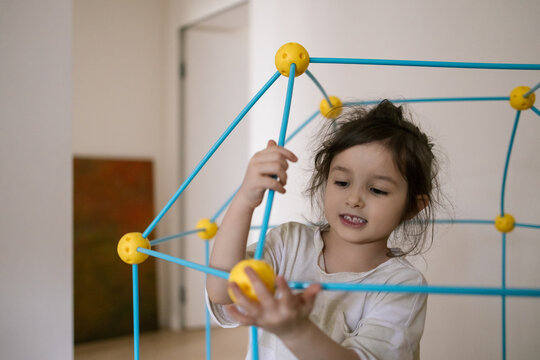 Little girl plays with colorful building toys indoors showing joyful focus and creative imagination in bright natural light