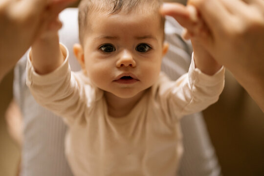 Tiny baby holds hands up as adult helps them stand up in warm home