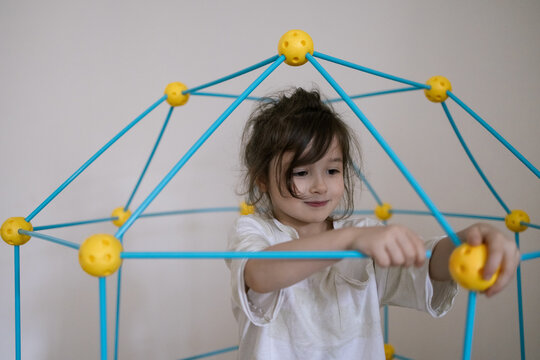 Young child plays with colorful geometric toy structure indoors showing joyful concentration and creativity in playtime moment