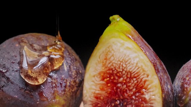 Sweet honey syrup pours and drips on ripe cut figs inside studio during detailed macro slow motion flight. Cinematic organic food video footage provides rich dark backdrop for design element.