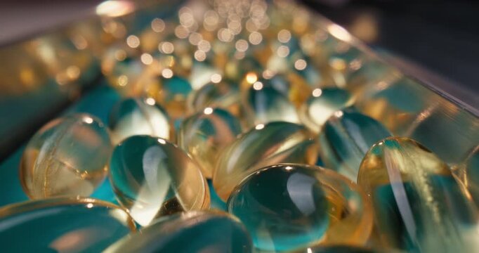 Slow motion softgel capsules sliding along blue conveyor belt in pharmaceutical production line inside factory.