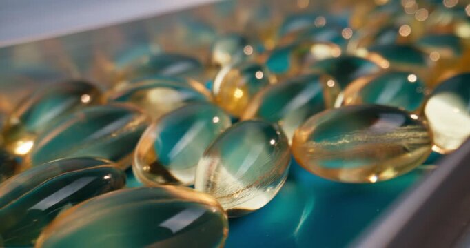 Slow motion softgel capsules sliding along blue conveyor belt in pharmaceutical production line inside factory.