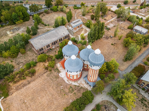 Aerial view of the restored air distillery towers and derelict brick industrial buildings at the historic Obuda gasworks in Budapest, Hungary, surrounded by dry grounds and trees.