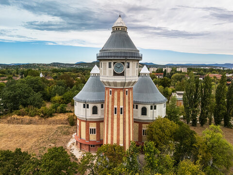 Aerial view of the restored historic gasworks tower at the former Obuda Gasworks, rising above trees and residential neighborhoods in Budapest, Hungary, on a summer day.