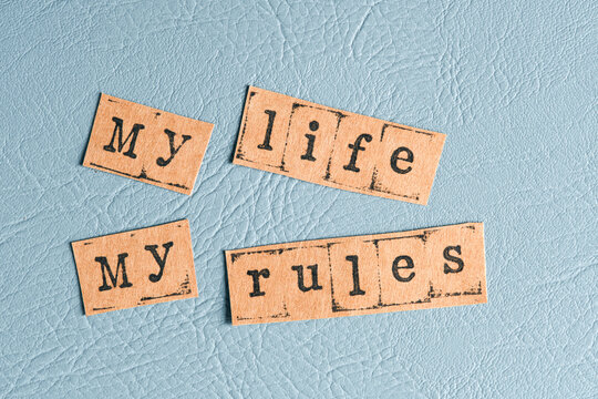 Cutout paper pieces forming phrase my life my rules scattered on blue leather texture.
