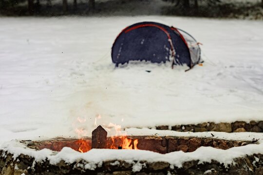 Tent and fire in winter snow landscape showcasing outdoor camping in cold conditions with smoke rising from the fire pit