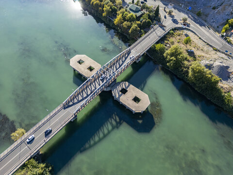 Aerial view of Ura e re e Bunes bridge spanning the turquoise waters of the Buna River with cars driving across and surrounding green vegetation in Shkoder, Qarku i Shkodres, Albania.
