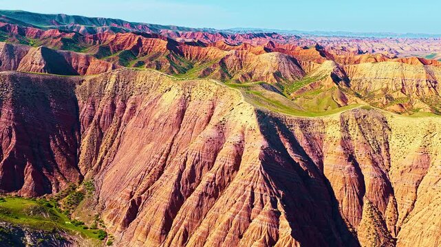 Vibrant colorful danxia landform in Xinjiang features dramatic red rock ridges and erosion textures under bright daylight.