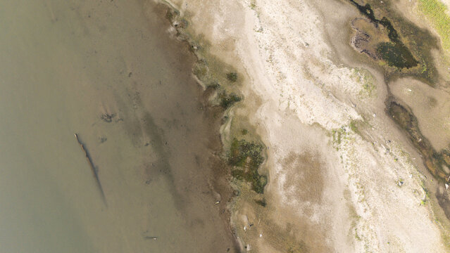 Aerial view of the Po River during a summer heatwave, showing low water levels with exposed sandy riverbed, sediment, and dry patches in Castelvetro Piacentino, Emilia-Romagna, Italy.