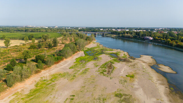 Aerial view of the Po River with low water levels due to drought and summer heatwave, exposing sediments, beaches, and the riverbed in Castelvetro Piacentino, Emilia-Romagna, Italy.