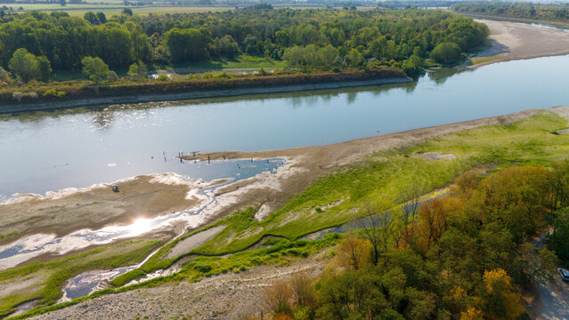 Aerial view of the Po River with low water levels caused by a summer heatwave and drought, exposing sandy riverbed sediments and beaches in Castelvetro Piacentino, Emilia-Romagna, Italy.