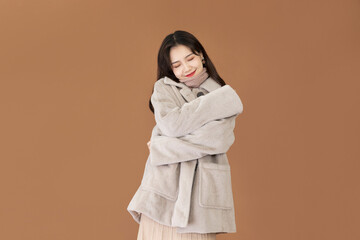 Happy Young Woman in Cozy Beige Fleece Coat Hugging Herself on Brown Background © CungDuc