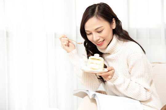 Happy Woman Eating Cake While Reading a Book at Home
