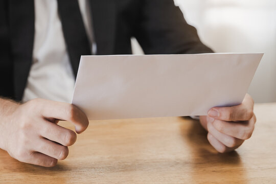 Close-up of Businessman in Suit Sitting at Desk and Holding White Paper Envelope resignation Letter