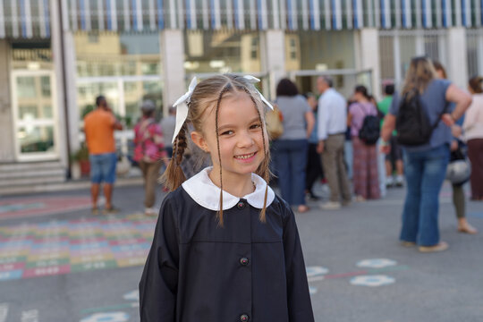Portrait of beautiful small girl with blonde hair with school building in background
