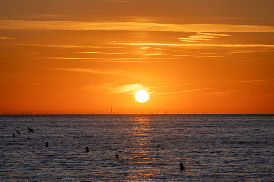 Luc-Sur-Mer, France - 08 08 2022:  Colorful sunrise over the sea and port of Le Havre far away
