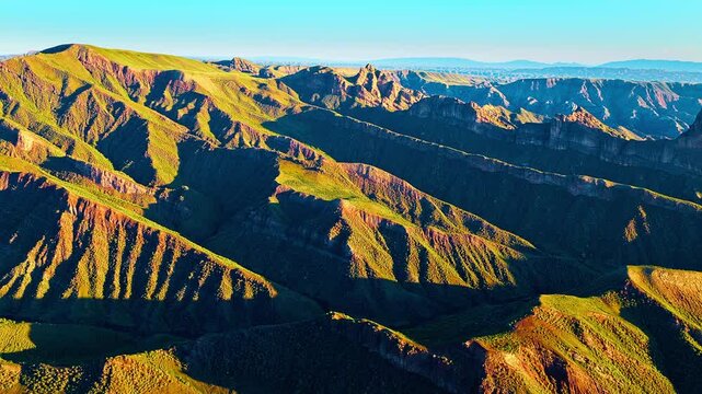 High angle view of dramatic mountain ridges covered in lush green grass and illuminated by warm sunlight during sunset.