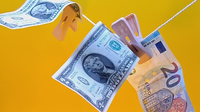 Various euro and dollar banknotes sway on clothespins.