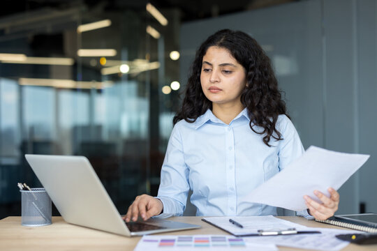 Professional businesswoman analyzing documents and typing on laptop