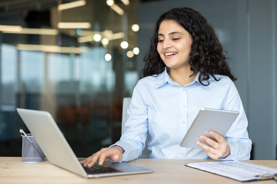 Smiling businesswoman working on laptop holding tablet