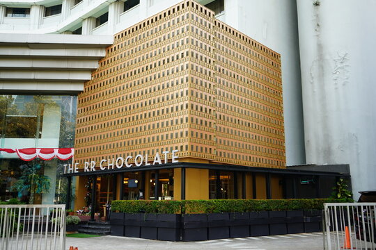 Modern exterior of store building with unique textured brown architectural facade, contemporary storefront design, elegant cafe entrance, and urban street view in Jakarta, Indonesia. (196 karakter ter