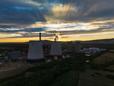 Aerial view of the lignite-fired Matra power plant with cooling towers and steam at sunset in Visonta, Hungary, surrounded by rural fields and the Matra hills.