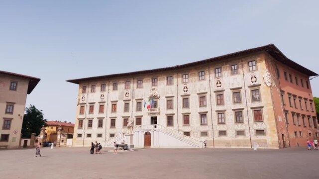 Static wide view of Palazzo della Carovana with flags above Piazza dei Cavalieri in sunshine, Pisa, Tuscany, Italy