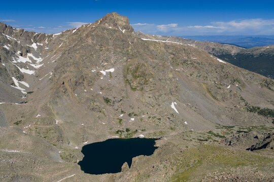 Aerial view of Mount of the Holy Cross in the Sawatch Range, featuring rugged rocky slopes, patches of snow, and a deep blue alpine lake in Vail, Colorado, United States.