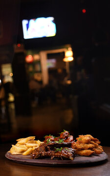 Close-up of a finger food platter featuring BBQ ribs, fried chicken, french fries, and buffalo wings on a table, with a blurred background.