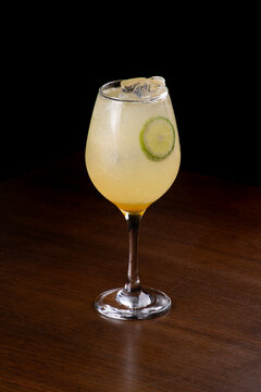Glass of gin limoncello spritz isolated on a wooden table, angled view, black background.