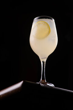 Glass of Limoncello Spritz isolated on a wooden table, low-angle shot against a black background, with a lemon.