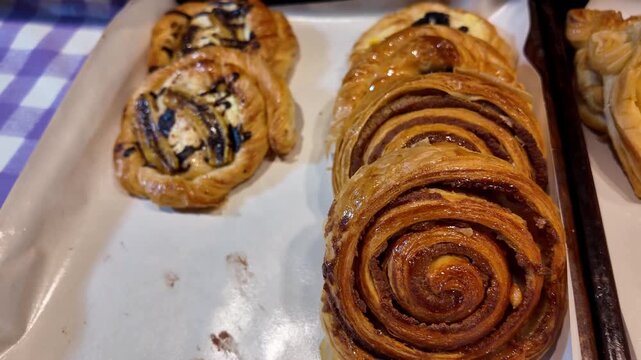 Close up shot of fresh baked cinnamon rolls and sweet danish pastry swirls displayed at a traditional street food market stall in Thailand.