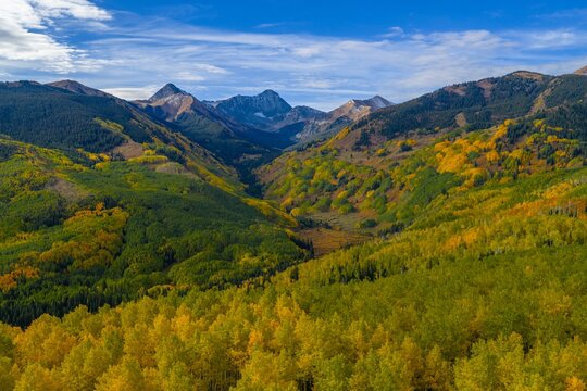 Aerial view of Capitol Peak and the Elk Range surrounded by vibrant autumn fall foliage and evergreen forests in the Rocky Mountains, Snowmass, Colorado, United States.