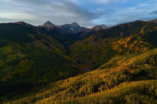 Aerial view of Capitol Peak and the Elk Range in the Rocky Mountains, featuring vibrant autumn fall foliage in the valley below at sunrise in Snowmass, Colorado, United States.