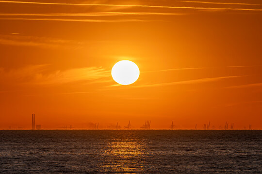 Luc-Sur-Mer, France - 08 08 2022:  Colorful sunrise over the sea and port of Le Havre far away