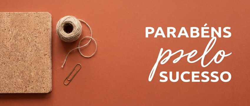 Portuguese congratulations banner parab&eacute;ns pelo sucesso with cork notebook, twine, and paperclip on terracotta background, top view flat lay for business achievement and professional success card head