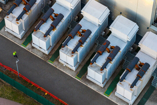 Aerial view of Kao Data industrial power generators and cooling units with a worker in a high-visibility jacket walking on the asphalt path in Harlow, England, United Kingdom.