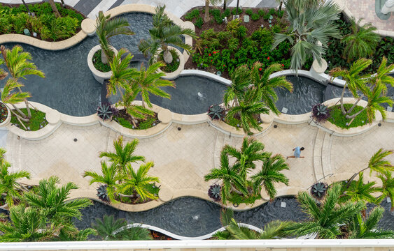 Aerial view of a landscaped courtyard with curved water features, lush palm trees, and stone walkways in Miami, Florida, United States.