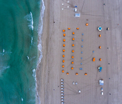 Aerial view of orange beach umbrellas arranged on the sandy shore with turquoise ocean waves lapping the coastline in Miami, Florida, United States.